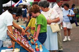 Two girls and a woman look at merchandise on a table, Lemonade Concert and Art Fair, St. Cloud State University