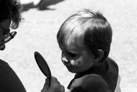 A boy looks in a mirror at his painted face, Lemonade Concert and Art Fair, St. Cloud State University