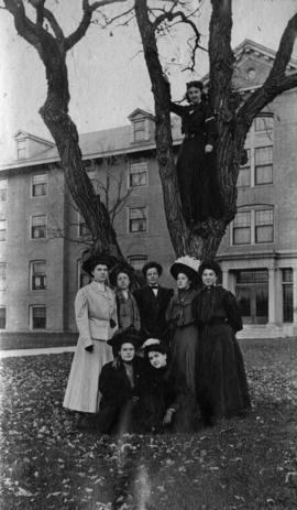 Women students gather around a tree outside of Lawrence Hall (1905), with Marie Petit in tree, St. Cloud State University