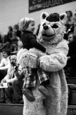 Husky mascot holds a child during a basketball game, St. Cloud State University