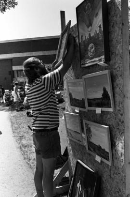 A man hangs up paintings, Lemonade Concert and Art Fair, St. Cloud State University