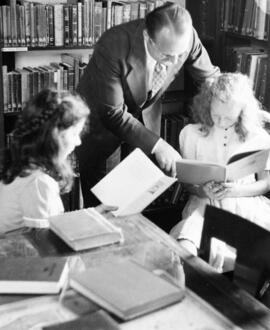 A teacher helps a student in the Riverview (1913) library, St. Cloud State University