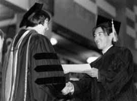 Barb Grachek hands a graduate a piece a paper at commencement, St. Cloud State University