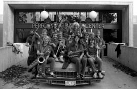 Jazz ensemble members sit together on a car hood in front of the Performing Arts Center (1968), St. Cloud State University