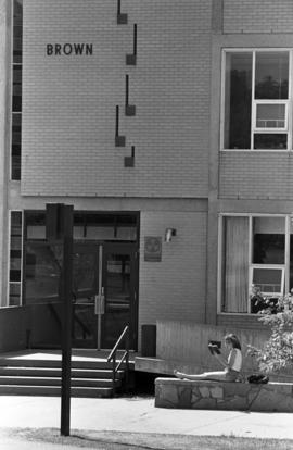 Woman sits outside of Brown Hall (1960) and reads a book