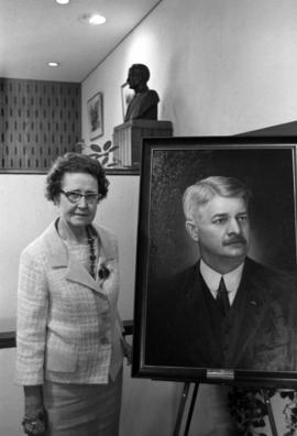 Ferne Atwood stands with a portrait of Clarence Atwood, St. Cloud State University