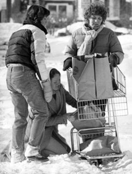 Joy Plaschko, Ann Smith, and Kim Brown navigate a grocery cart through the snow